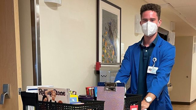 Young person pushing a cart of activity items in hospital hallway